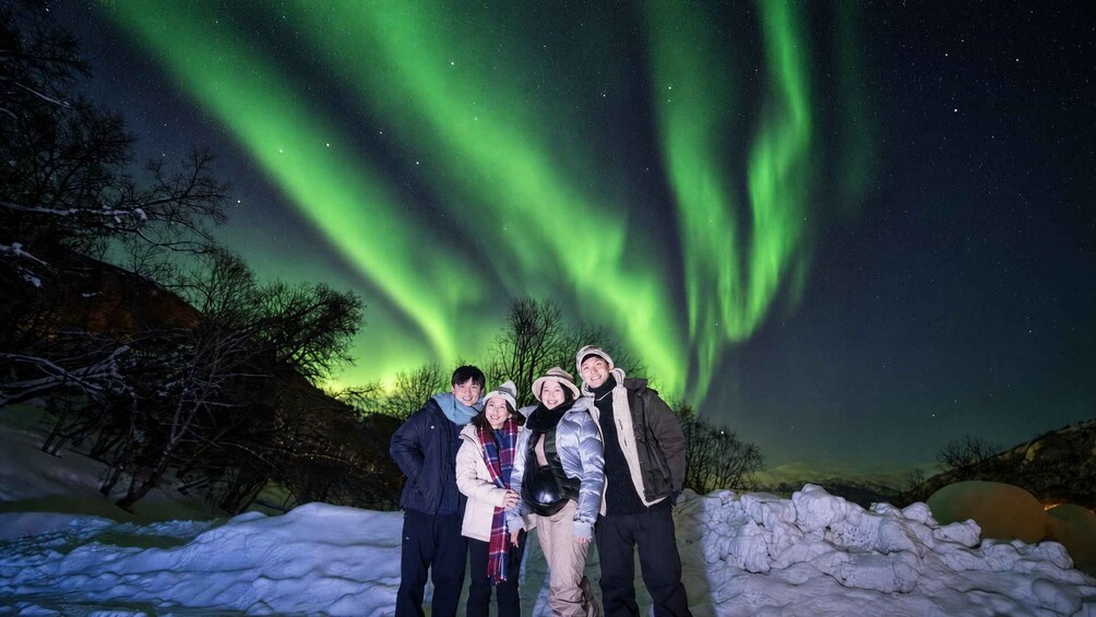 A group of people standing on snow-covered ground with the aurora borealis in the background. 3