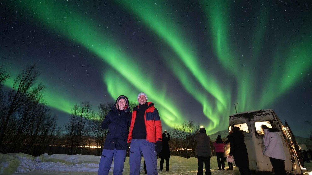 A couple posing under the aurora borealis with people around them. 2