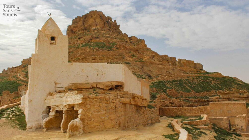 An ancient ruin with a small tower, surrounded by rugged terrain and sparse vegetation. 5
