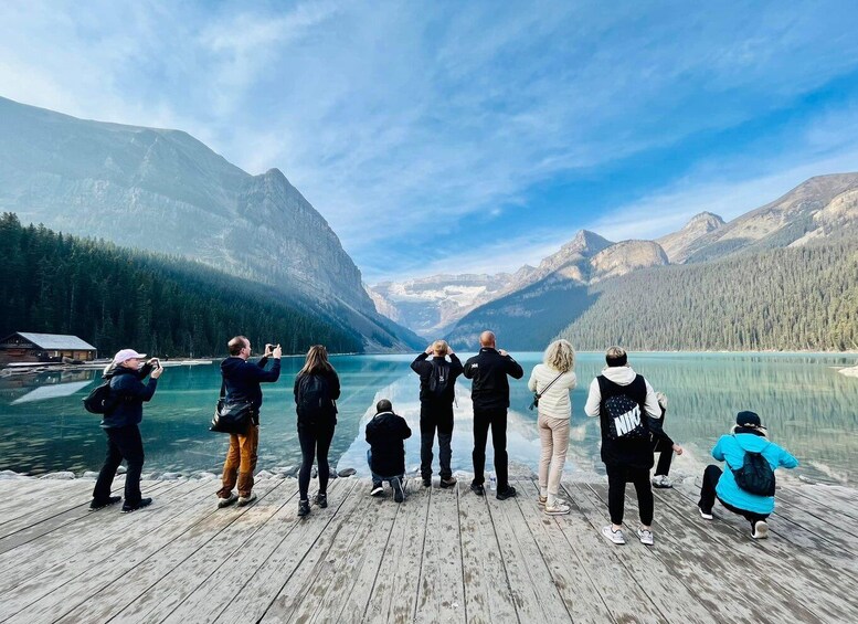 A group of people on a wooden dock overlooking a calm lake with mountains in the background. 1