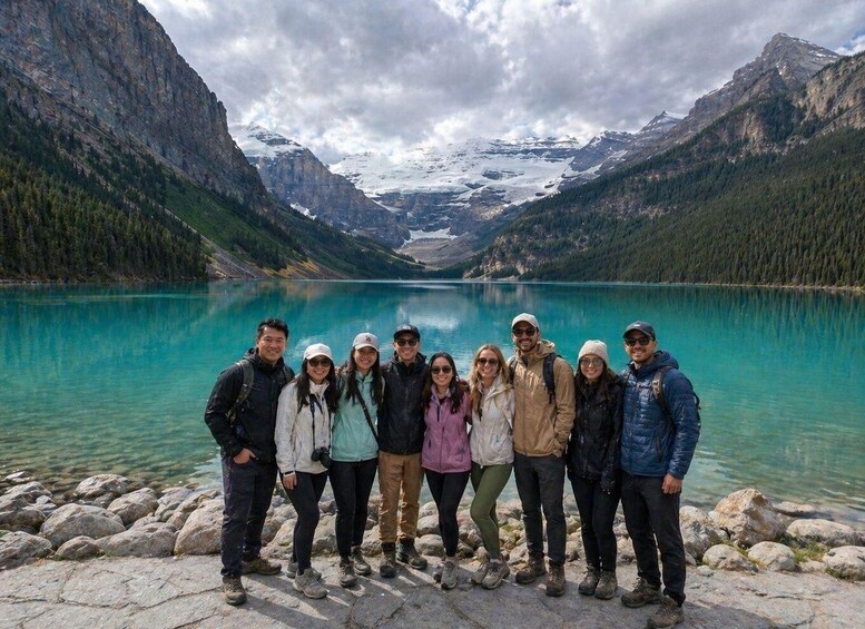 A group of people standing by a turquoise lake surrounded by mountains. 3