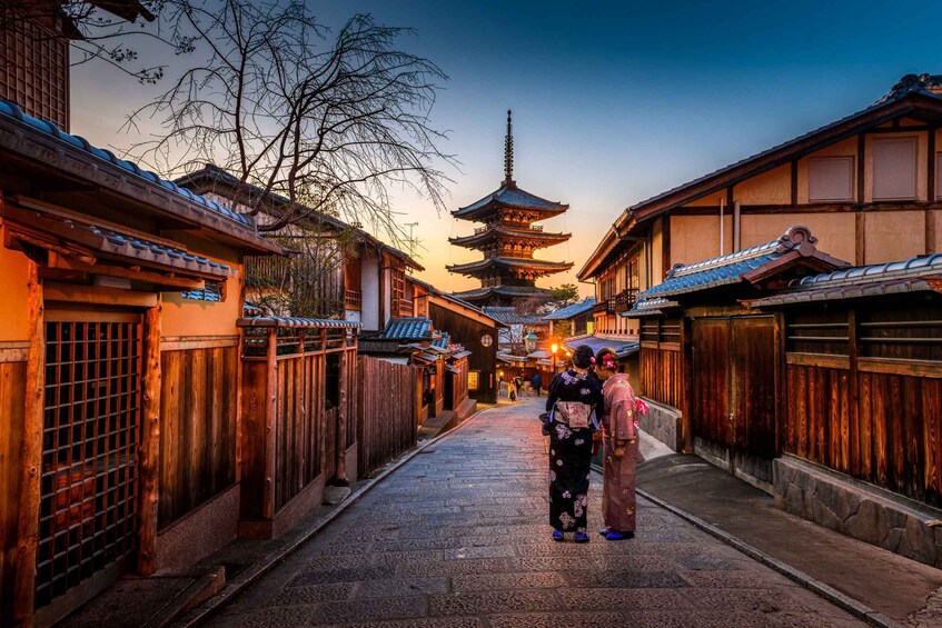 A traditional Japanese street with wooden buildings, a pagoda, and two people in traditional attire. 1