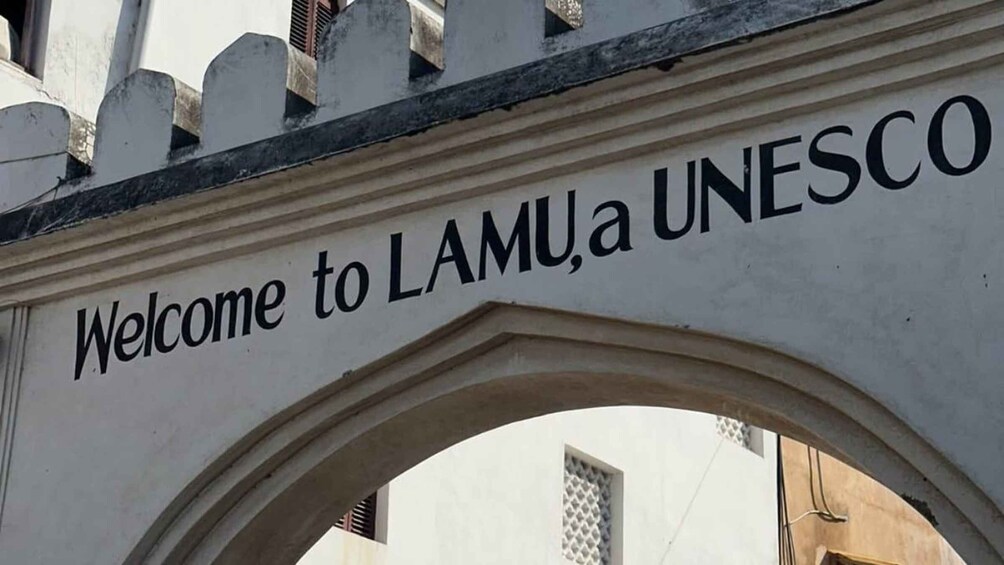 A sign with the text 'Welcome to LAMU, a UNESCO' above an arched entrance. 5