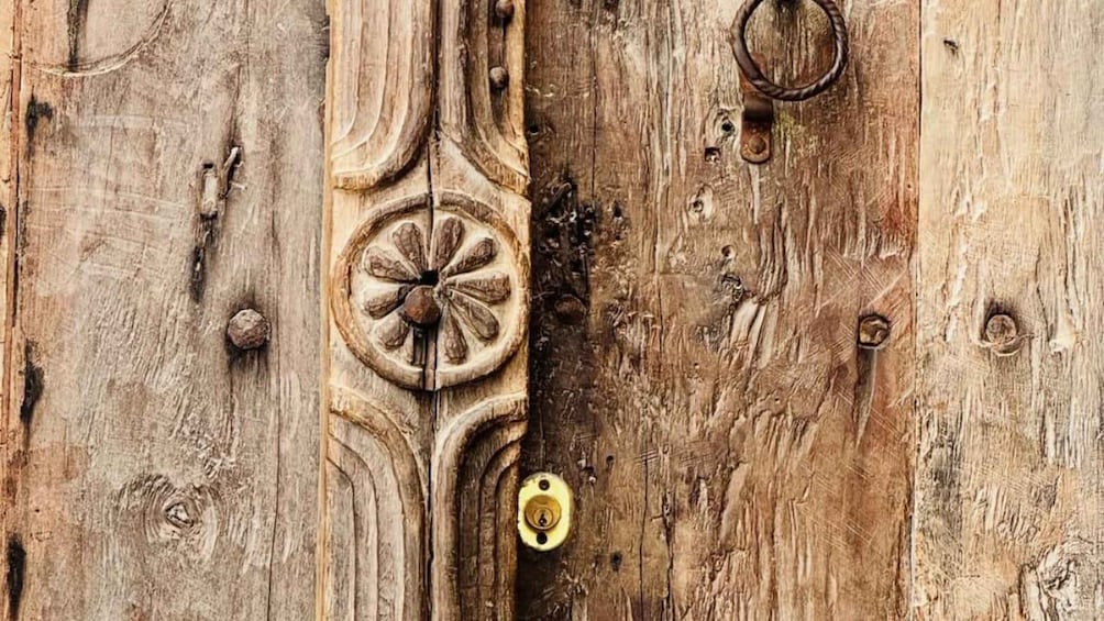 A weathered wooden surface with a circular carved design, a brass padlock, and a metal ring. 1