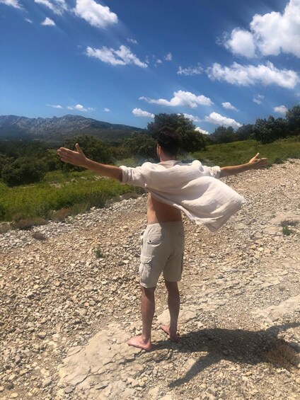 A person standing on a rocky terrain with arms outstretched, facing a mountainous landscape. 1