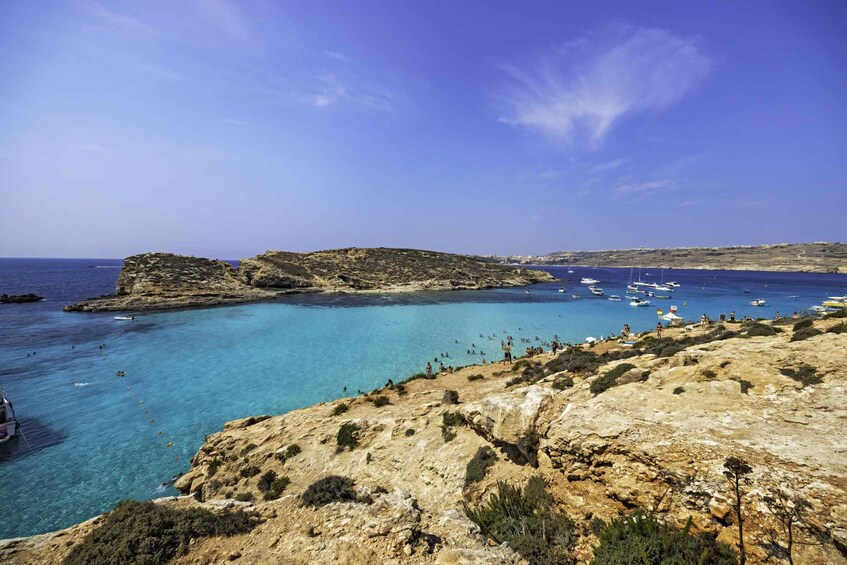 A coastal landscape with clear blue waters, rocky cliffs, and boats in the distance. 3