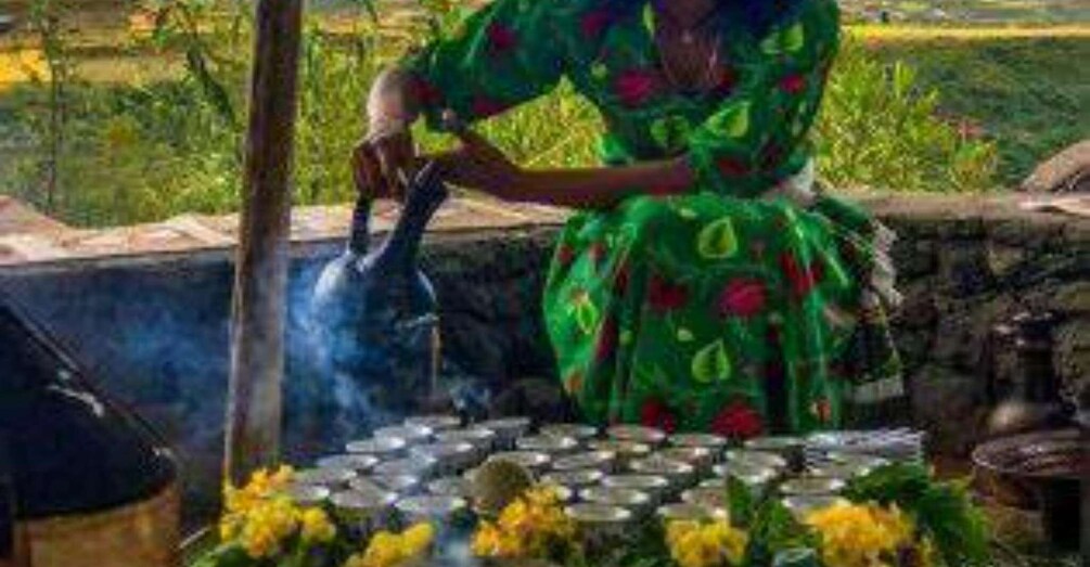 A person in a green dress pouring water from a jug into a metal container. 2