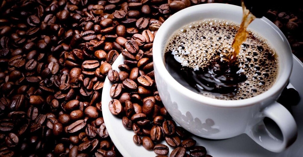 A cup of coffee with a spoon pouring into it, surrounded by coffee beans. 1