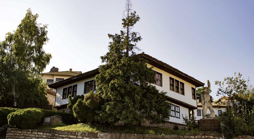 A white house with a red roof, surrounded by trees and a stone wall. 2