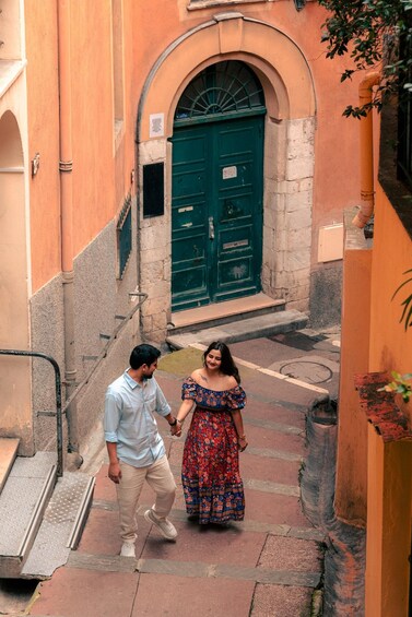 A narrow alleyway with a green door, a man and a woman walking, and a building with orange walls. 3