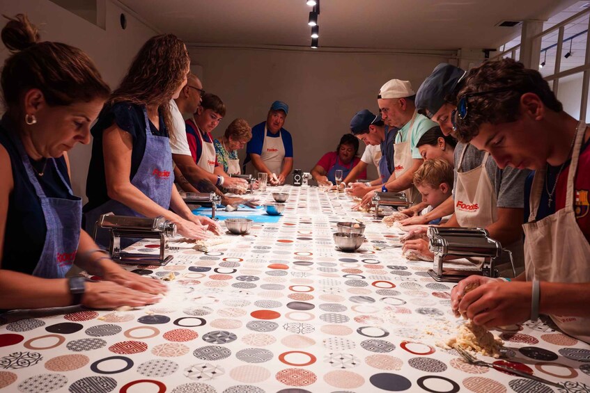 A group of people engaged in a cooking activity, wearing aprons, and using various kitchen tools and ingredients on a table with a patterned tablecloth. 1