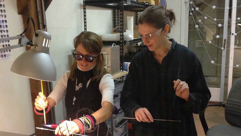 Two people working with a light source and a rod, possibly in a laboratory or workshop setting. 2