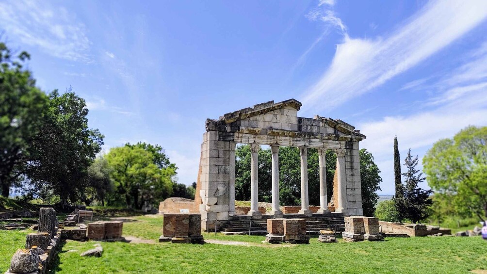 Ancient ruins with columns and stone structures in a grassy area. 1