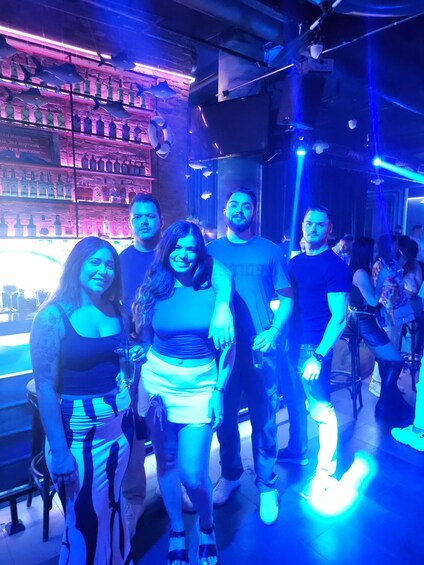 A group of people in a bar with shelves of liquor bottles and blue lighting. 1