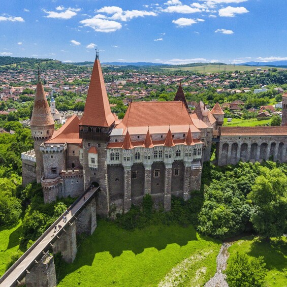 A castle with a red-tiled roof, surrounded by lush greenery and a river. 1