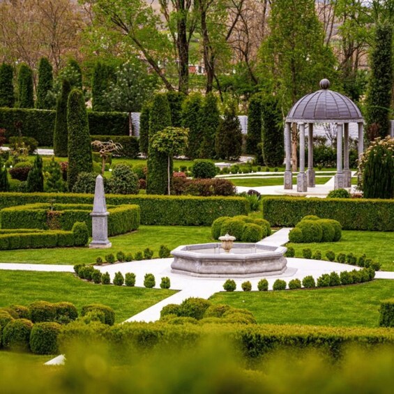 A formal garden with a central fountain, trimmed hedges, and a gazebo. 5