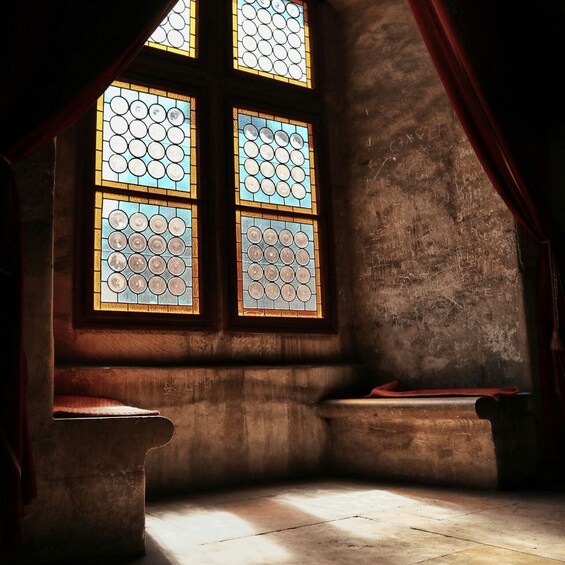 A room with four stained glass windows, a stone bench, and a red curtain. 3