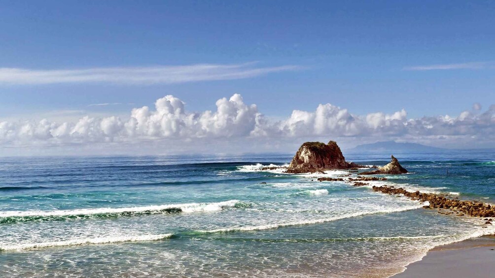 A beach with waves, a rocky outcrop, and a clear sky. 2