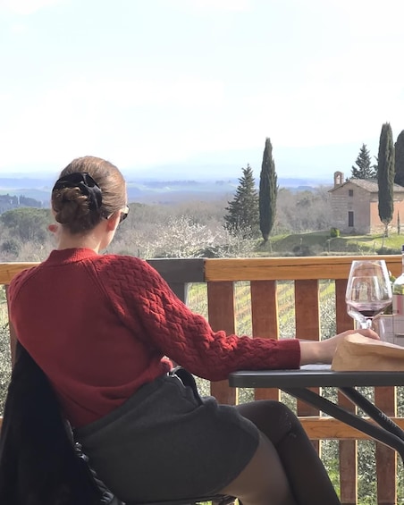 A person seated on a wooden deck overlooking a landscape with trees and a distant building. 1