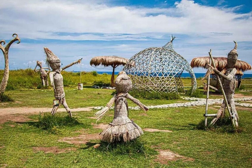 A grassy field with straw sculptures of figures and a large geometric structure. 2