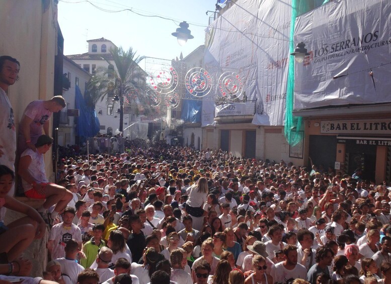 A crowded street with people gathered, buildings, and a large banner. 5
