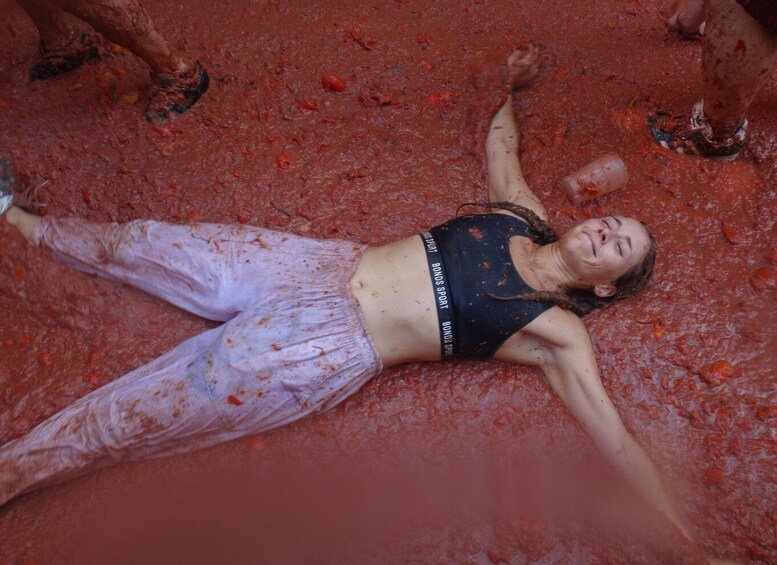 A person lying on the ground covered in red mud. 2