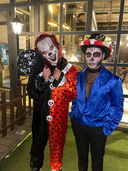 Kaksi henkilöä, joilla on päällään Halloween-aiheiset asut, seisoo suuren ikkunapintainen rakennuksen edessä. 2