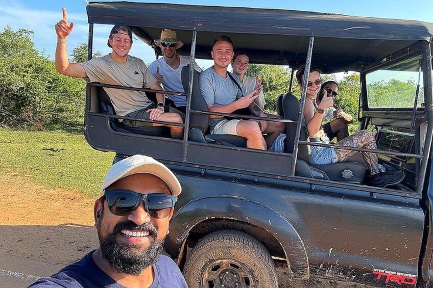 A group of people in a safari vehicle on a dirt road with greenery in the background. 2