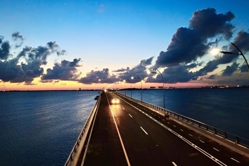 A bridge at sunset with road lights, water, and clouds. 3