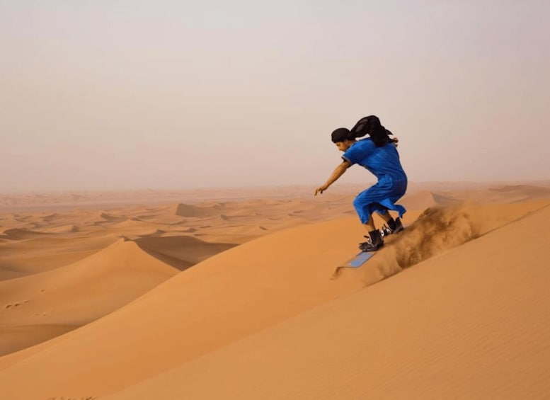 A person in blue attire riding a board down a sand dune. 2
