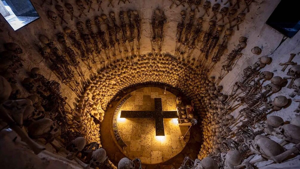 A circular crypt with a cross at the center, surrounded by skeletons and skulls. 4