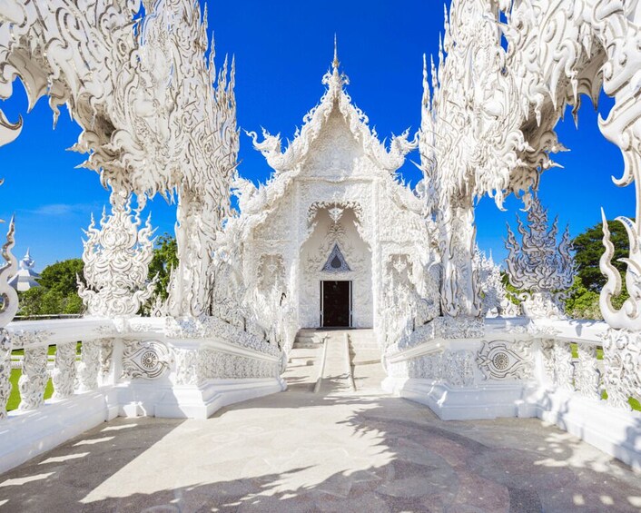A white ornate temple with intricate carvings and a clear blue sky. 1
