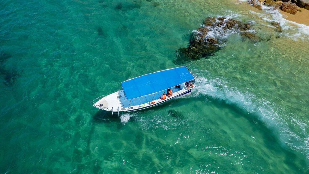 A boat with a blue canopy sailing near a rocky shore. 3