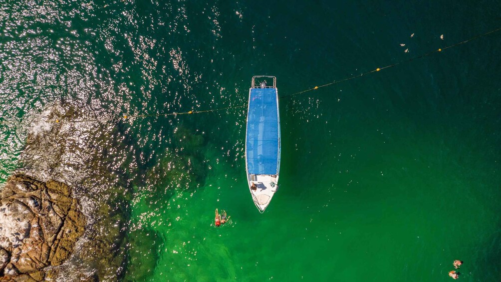 An aerial view of a boat anchored near a rocky coastline with clear green water. 4