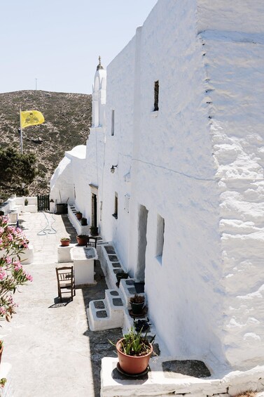 A white-washed building with a flag, potted plants, and a chair. 5