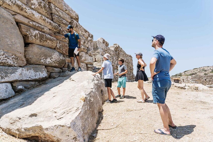 A group of people standing on a stone platform with a large rock wall behind them. 4