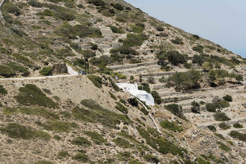 A hillside with white-roofed buildings, a dirt path, and sparse vegetation. 3
