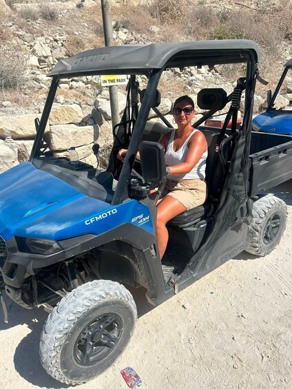 A person in a blue CFMOTO 4x4 vehicle parked in a rocky outdoor area. 3
