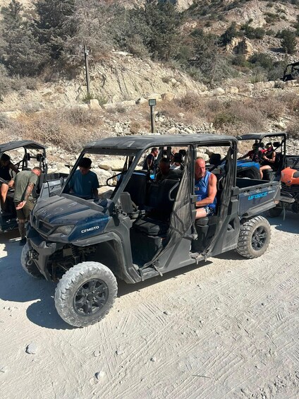 A UFORCE 1000XL off-road vehicle with passengers, parked on a dirt road with rocky terrain and sparse vegetation in the background. 4