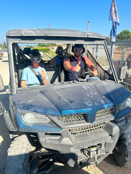 A CFMOTO off-road vehicle with two people inside, one driving and one passenger, at a fenced outdoor area. 2