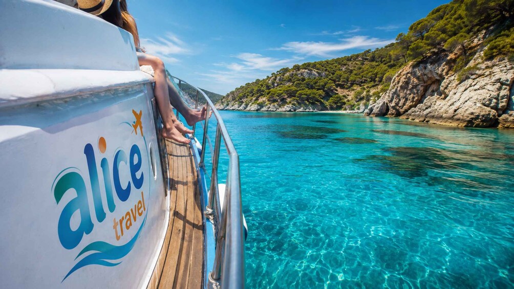 Ein Boot mit der Aufschrift 'alice travel', klares blaues Wasser, eine felsige Küste und ein klarer Himmel. 1