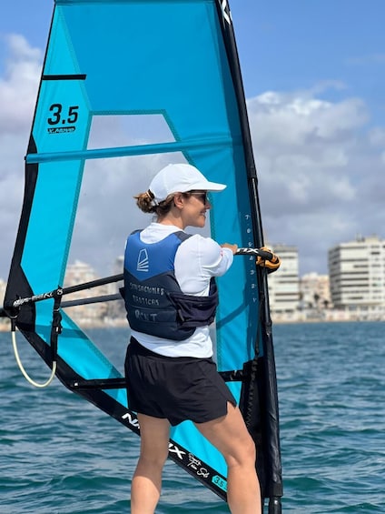 A person windsurfing on a body of water with buildings in the background. 1