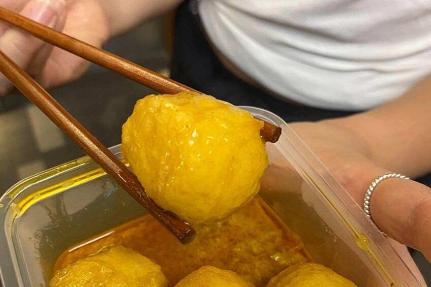 A person holding a yellow dumpling with chopsticks over a container of similar dumplings. 2
