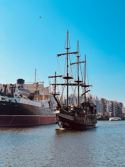 A tall ship docked at a harbor with buildings in the background. 1