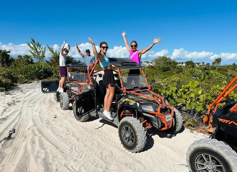 Four people on off-road vehicles on a sandy path with vegetation in the background. 2