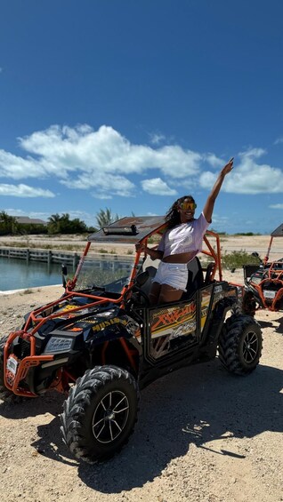 A person in a white shirt and shorts riding an ATV on a sandy beach with a clear sky. 3