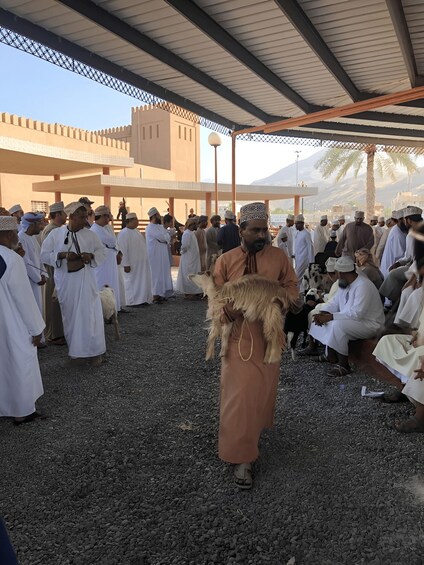 A group of people in traditional attire gathered under a covered area with a mountainous backdrop. 4