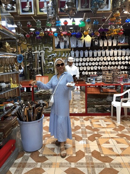 A person in a blue dress standing in a shop with various items on display, including hanging ornaments and jewelry. 2