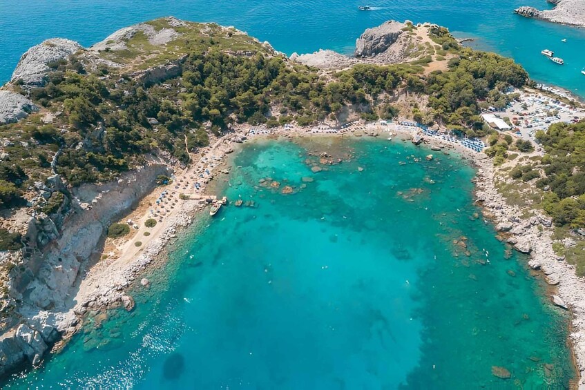 A coastal area with clear turquoise waters, rocky terrain, and a small beach with people and boats. 4