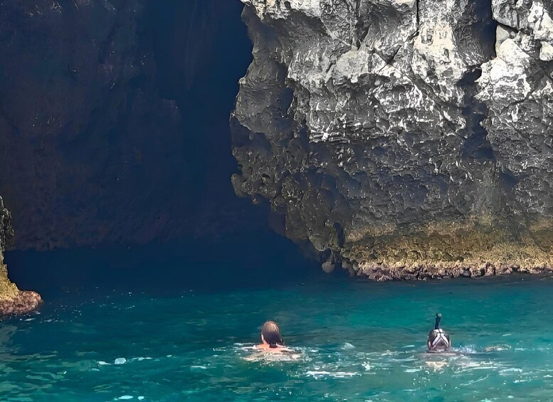 A person swimming in clear blue water with a rocky cliff in the background. 5